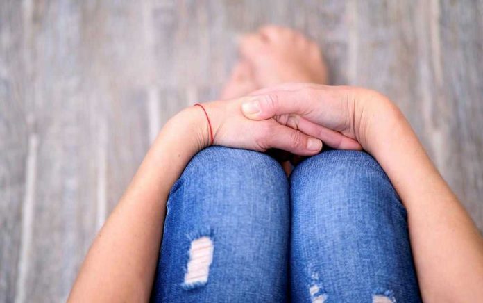 Person sitting with folded hands on knees.
