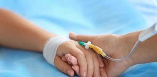 Two hands holding, one with medical IV attached.