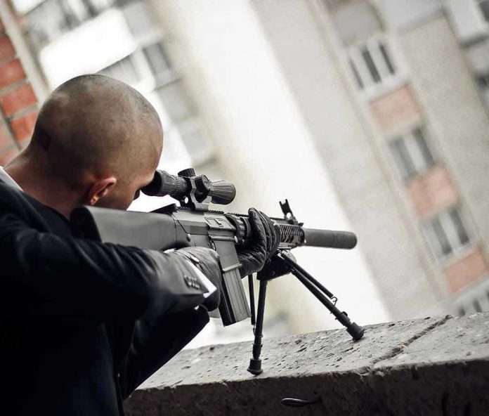 Person aiming a rifle from a building balcony.