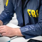 Person in FBI jacket typing on a laptop