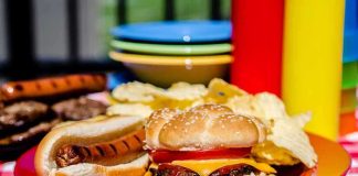 A plate with a hamburger, hot dog, and potato chips on a picnic table