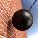 A wrecking ball suspended near a brick wall, suggesting demolition activity