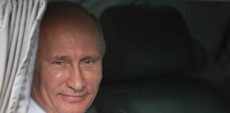 A smiling man in formal attire sitting inside a car with curtains
