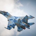 A blue camouflage fighter jet performing an aerial maneuver against a cloudy sky