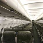 Empty airplane cabin with rows of green seats.