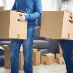 Two people carrying cardboard boxes indoors.