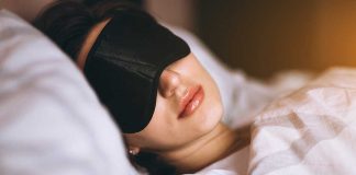 Woman sleeping with a black sleep mask in a cozy bed