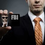 A man in a suit holding an FBI identification card while making a shushing gesture