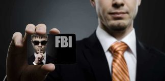A man in a suit holding an FBI identification card while making a shushing gesture