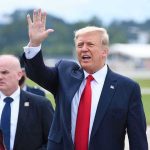 Trump Pulled The Curtain Back On Walz Man in suit waving while another man stands nearby.