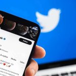 Hand holding phone displaying Twitter profile.