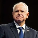 Walz’s Holocaust Horror Stuns Museum Man in suit with a U.S. flag pin.