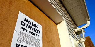 Sign on a boarded-up property indicating it is bank owned and warns to keep out