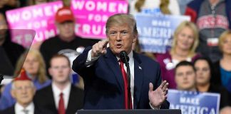 Person speaking at rally with crowd behind podium