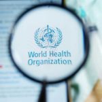 WHO Sounded the Alarm — Why Now? Magnifying glass focused on World Health Organization logo.
