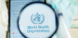 WHO Sounded the Alarm — Why Now? Magnifying glass focused on World Health Organization logo.