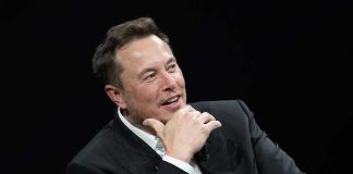 Musk Blasts College Degrees—$200K for Homework? Man in suit smiling, resting chin on hand.