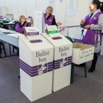 Polis Defies Critics: Halves Trump Ally’s Sentence Election polling station with ballot boxes and officials.