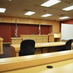 Judge’s Ruling Splits Mangione Case Wide Open Interior view of an empty courtroom with wooden furniture and American flags