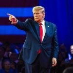 Trump’s LATEST PICK Sparks Firestorm — WHERE’S THE BEEF? Person in suit pointing during a public event.