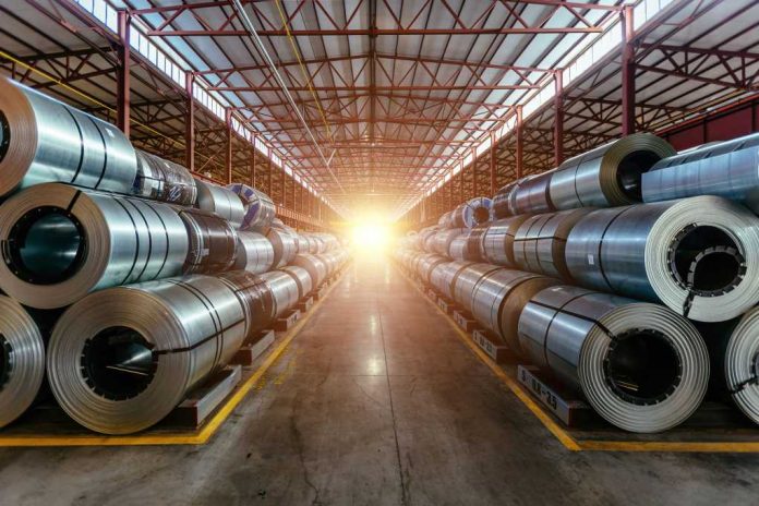 shutterstock2119130636jpg-1 Interior of an industrial warehouse filled with stacked metal coils and sunlight streaming in