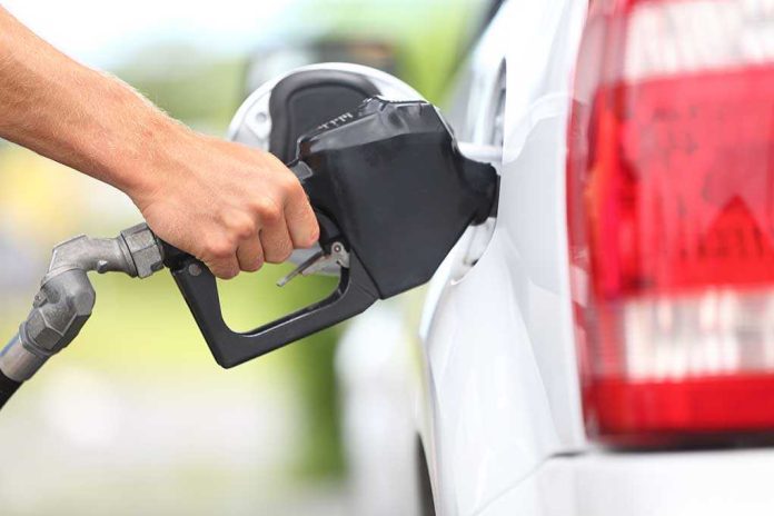 A hand holding a fuel nozzle while refueling a white vehicle at a gas station