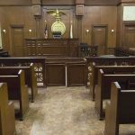 Historic First — HORRIFYING Fall FROM GRACE Interior view of an empty courtroom with wooden benches and a judges bench