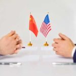 Trump’s NEW China Deal — Did He REALLY DO THAT? Two hands of individuals facing each other with flags of China and the USA on the table