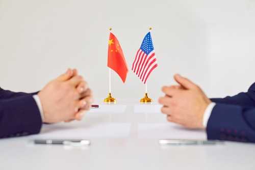 Two hands of individuals facing each other with flags of China and the USA on the table