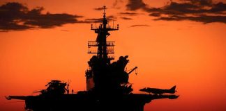 Silhouette of a naval aircraft carrier against a vibrant sunset