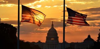 Silhouetted American flags in front of the Capitol building during sunset