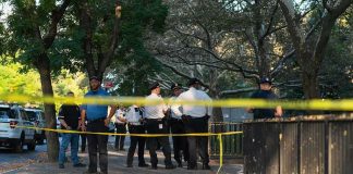 Pool SCARE Tied To GABBARD Police officers gather behind yellow tape on a tree-lined sidewalk