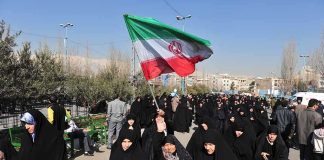 BRUTAL — Iran’s HAIR POLICE Goes High-Tech Group of women in black attire marching with an Iranian flag
