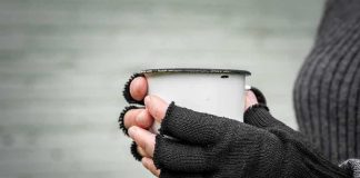 Hands in fingerless gloves holding a white metal mug