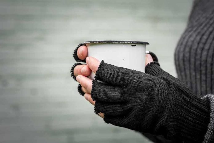 Hands in fingerless gloves holding a white metal mug
