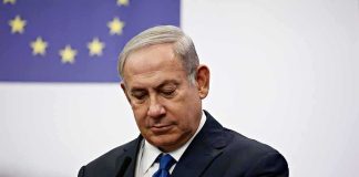 Interpol Bombshell TARGETS Netanyahu man in suit at podium with EU flag in background