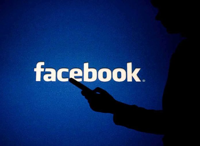 silhouette holding a smartphone in front of Facebook logo