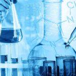 Scientist holding a flask with blue liquid and pipette over test tubes