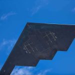 Stealth aircraft wing seen from below against blue sky