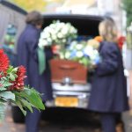 Funeral flowers with hearse and people in background
