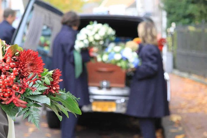 Funeral flowers with hearse and people in background