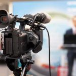 Harassment BOMBSHELL Hits CBS Star video camera filming a speaker at a podium