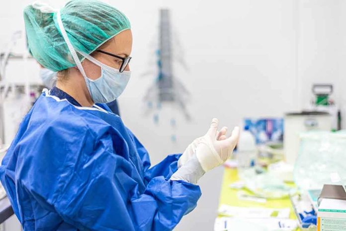 shutterstock_1680760828 medical professional in blue gown putting on sterile gloves
