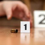 TWO Bodies, One Day — CITY on Edge Bullet casing beside evidence marker 1 on floor