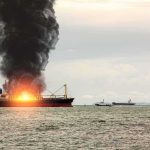 Cargo ship on fire with thick black smoke at sea