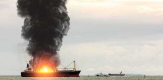 Cargo ship on fire with thick black smoke at sea
