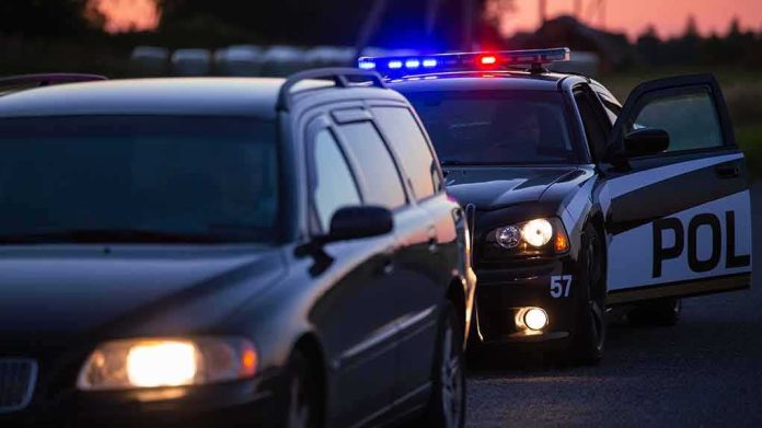 shutterstock_2232051647 Police car with flashing lights behind a stopped vehicle at dusk