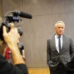 Man in a gray suit speaks to a reporter during an interview