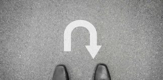Feet in black shoes facing a U-turn arrow on asphalt