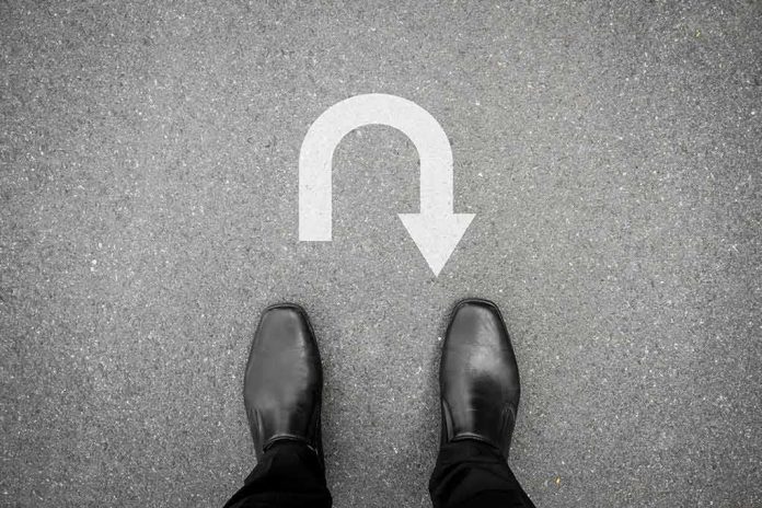 Feet in black shoes facing a U-turn arrow on asphalt